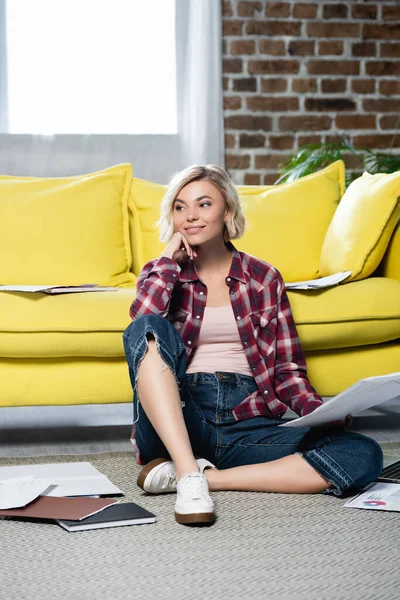 Young blonde woman in checkered shirt sitting on floor with documents — Stock Photo