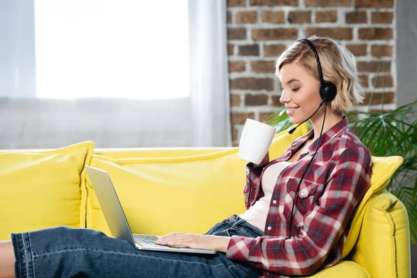 Giovane donna bionda con webinar seduto a casa e bere tè — Foto stock