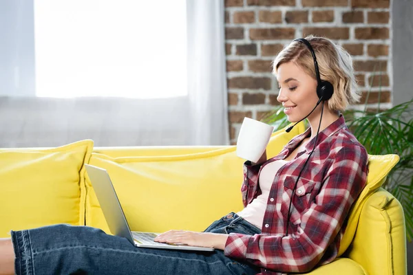 Young blonde woman having webinar sitting at home and drinking tea — Stock Photo