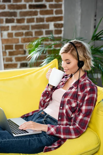 Young blonde woman having webinar sitting at home and drinking tea — Stock Photo