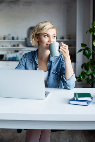 Young blonde woman working from home and drinking tea — Stock Photo