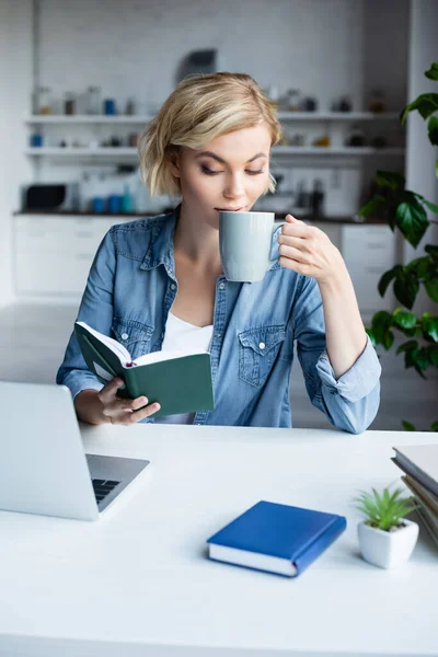 Junge blonde Frau arbeitet von zu Hause aus und trinkt Tee — Stockfoto