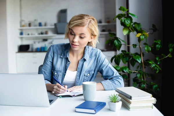Young blonde woman studying online and making notes — Stock Photo