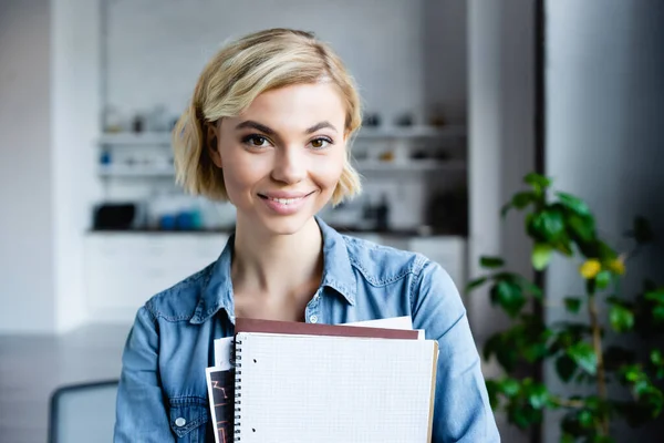 Young blonde woman holding notebooks at home — Stock Photo