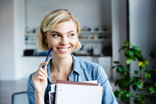 Junge blonde Frau hält Stift und Notizbücher zu Hause — Stockfoto