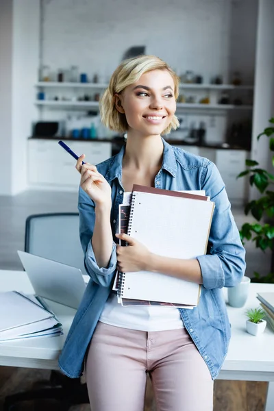 Junge blonde Frau hält Stift und Notizbücher zu Hause — Stockfoto