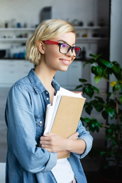 Young blonde woman in eyeglasses holding notebooks at home — Stock Photo