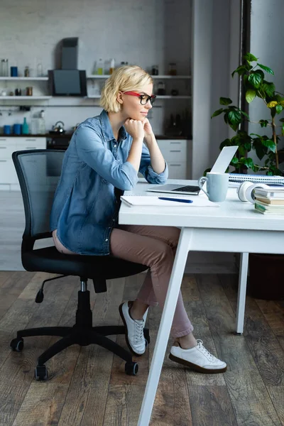 Comprimento total de jovem loira em óculos trabalhando em casa — Fotografia de Stock