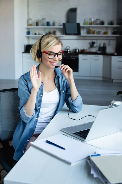 Joven rubia mujer en gafas teniendo videollamada y saludando la mano - foto de stock