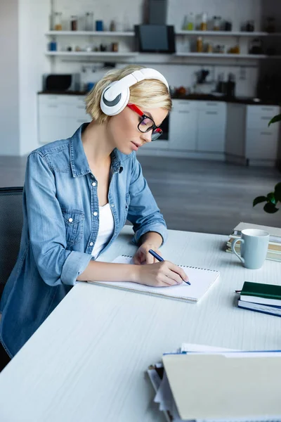 Young blonde woman in eyeglasses writing notes in notebook — Stock Photo