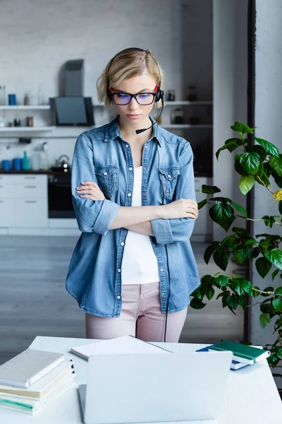 Jeune femme blonde dans des lunettes avec les bras croisés regardant ordinateur portable — Photo de stock