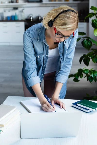 Junge blonde Frau mit Brille schreibt Notizen in Notizbuch — Stockfoto