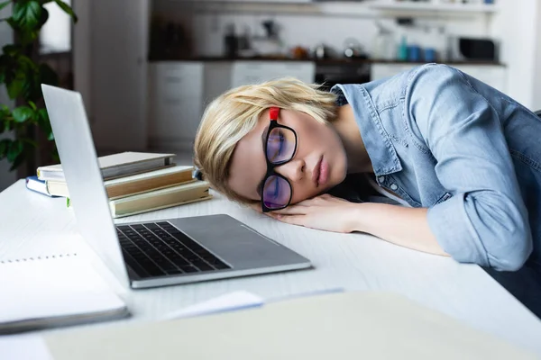 Joven mujer rubia en gafas de vista durmiendo en el escritorio en casa - foto de stock