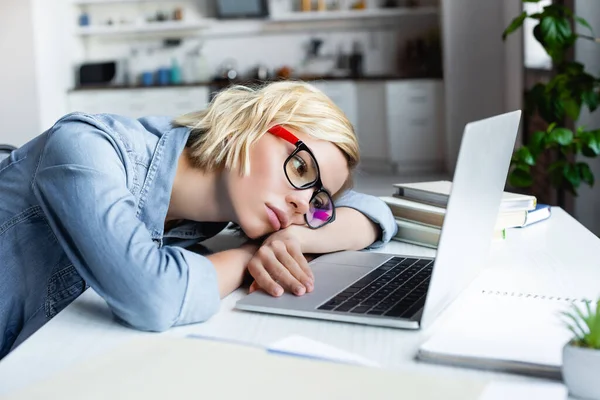 Tired blonde woman in eyeglasses working from home and lying on table — Stock Photo