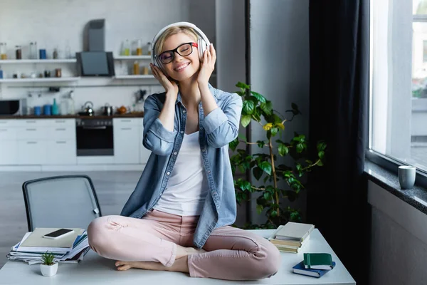 Jeune femme blonde à lunettes écouter de la musique et assis sur la table — Photo de stock