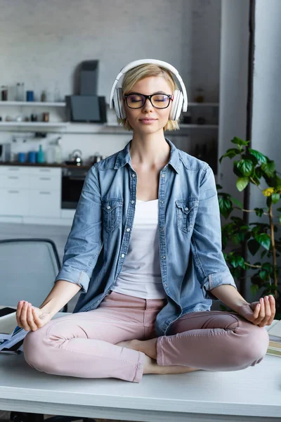 Junge blonde Frau mit Brille sitzt in Lotus-Pose auf Tisch — Stockfoto