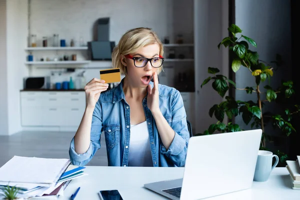 Impactado mujer rubia en gafas haciendo compra en línea - foto de stock