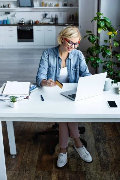 Young blonde woman in eyeglasses making purchase online — Stock Photo