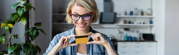 Young blonde woman in eyeglasses holding credit card, horizontal banner — Stock Photo