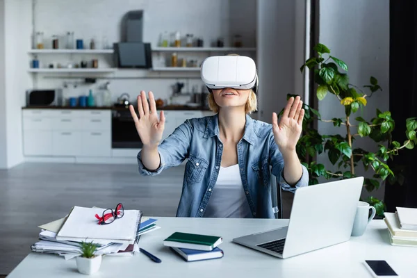 Blonde woman in vr headset gesturing while sitting at table — Stock Photo