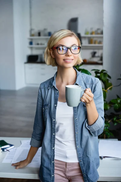 Молодая блондинка в очках пьет чай дома — стоковое фото