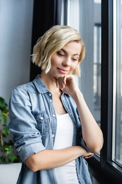 Retrato de mujer pensativa de pie cerca de la ventana - foto de stock