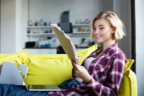 Blonde woman in checkered shirt working from home and looking through documents — Stock Photo