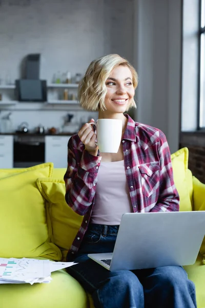 Blonde woman in checkered shirt working from home and drinking tea — Stock Photo