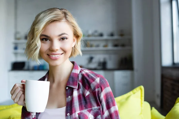 Femme blonde souriante en chemise à carreaux tenant une tasse blanche — Photo de stock