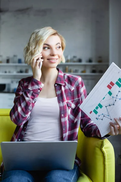 Joven rubia en camisa a cuadros sosteniendo documentos y hablando en el teléfono inteligente - foto de stock