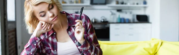 Bored blonde woman in checkered shirt holding pen, banner — Stock Photo