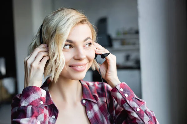 Junge blonde Frau im karierten Hemd setzt Kopfhörer auf — Stockfoto