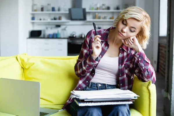 Femme blonde ennuyée en chemise à carreaux tenant stylo et regardant des notes — Photo de stock
