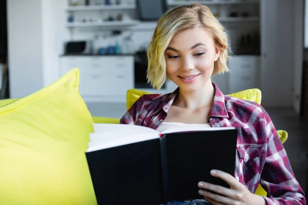 Mujer rubia joven en camisa a cuadros buscando en cuaderno - foto de stock