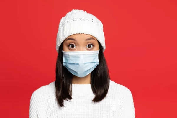 Shocked asian woman in medical mask and hat isolated on red — Stock Photo