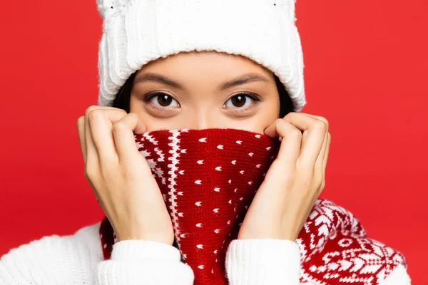 Joven asiático mujer en blanco sombrero cubriendo la cara con rojo bufanda con ornamento aislado en rojo - foto de stock