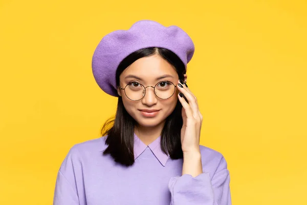 Happy asian woman in beret adjusting eyeglasses isolated on yellow — Stock Photo