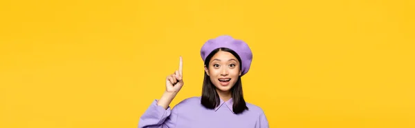 Mujer asiática feliz en boina señalando con el dedo aislado en amarillo, bandera - foto de stock