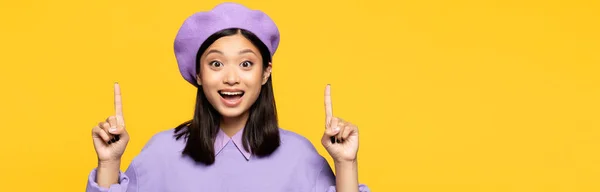 Mujer asiática feliz en boina señalando con los dedos aislados en amarillo, bandera - foto de stock