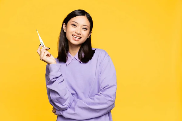Mujer asiática feliz sosteniendo termómetro digital aislado en amarillo - foto de stock