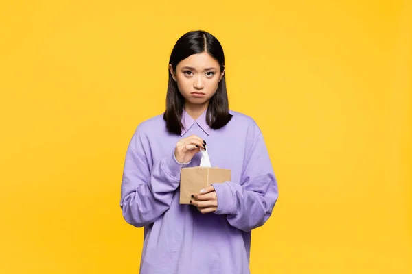 Sad asian woman holding tissue box isolated on yellow — Stock Photo