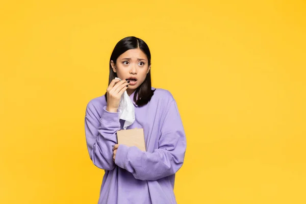 Schockierte asiatische Frau hält Gewebebox in der Hand und schaut isoliert auf gelb weg — Stockfoto
