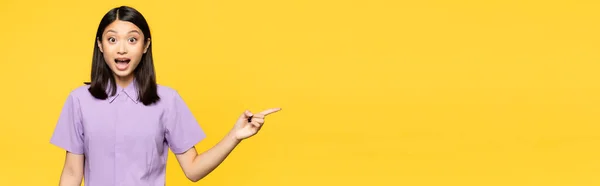 Excited asian woman with open mouth pointing with finger isolated on yellow, banner — Stock Photo