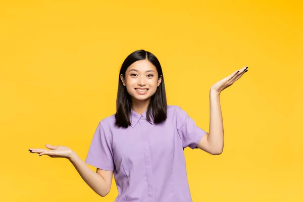 Happy asian woman pointing with hands isolated on yellow — Stock Photo