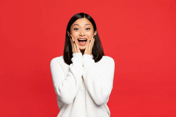 Excited asian woman with open mouth touching cheeks isolated on red — Stock Photo