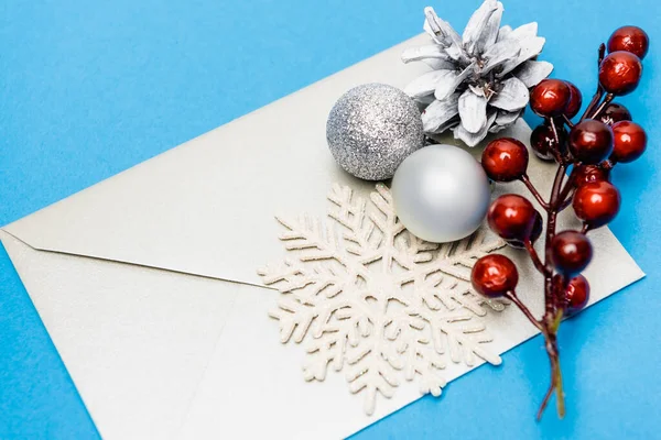 Snowflake, silver baubles, berries and envelope on blue background — Stock Photo