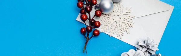 Top view of snowflake, silver baubles, berries and envelope on blue background, banner — Stock Photo