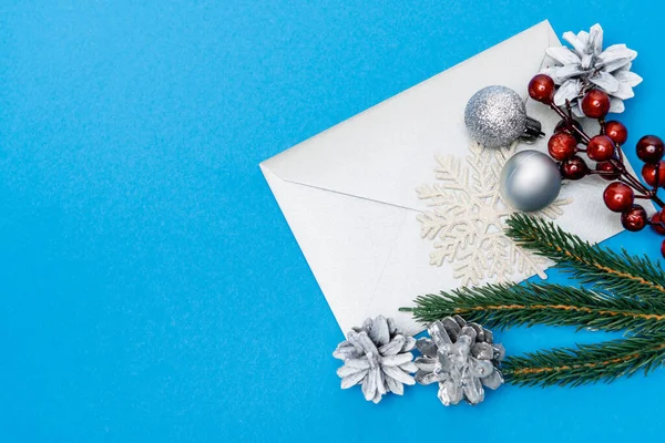 Top view of snowflake, silver baubles, berries, spruce and envelope on blue background — Stock Photo