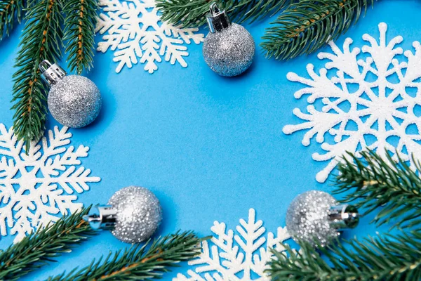 Вид сверху на снежинки, серебряные безделушки и ель на голубом фоне — стоковое фото