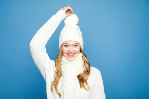 Feliz rubia hermosa mujer en invierno blanco traje tocando pom pom sobre fondo azul - foto de stock